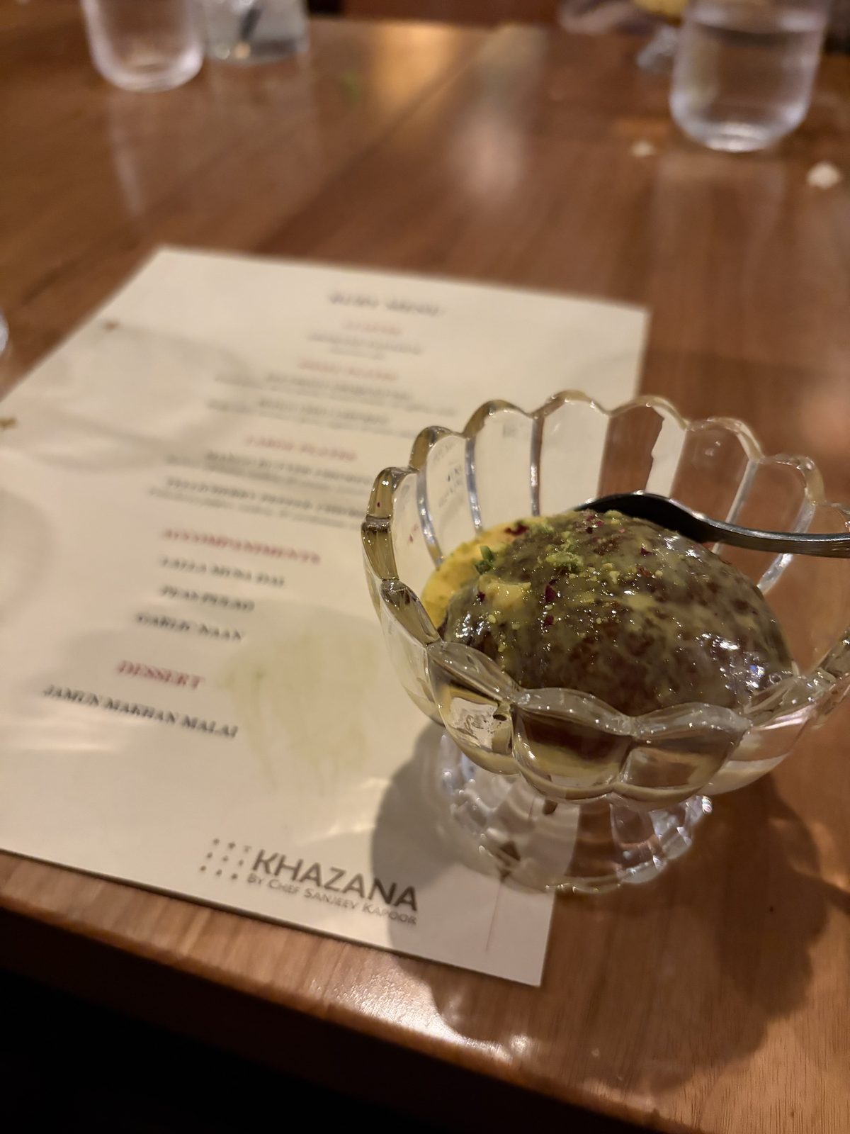 Jamun makhan malai in a glass dessert bowl beside the menu