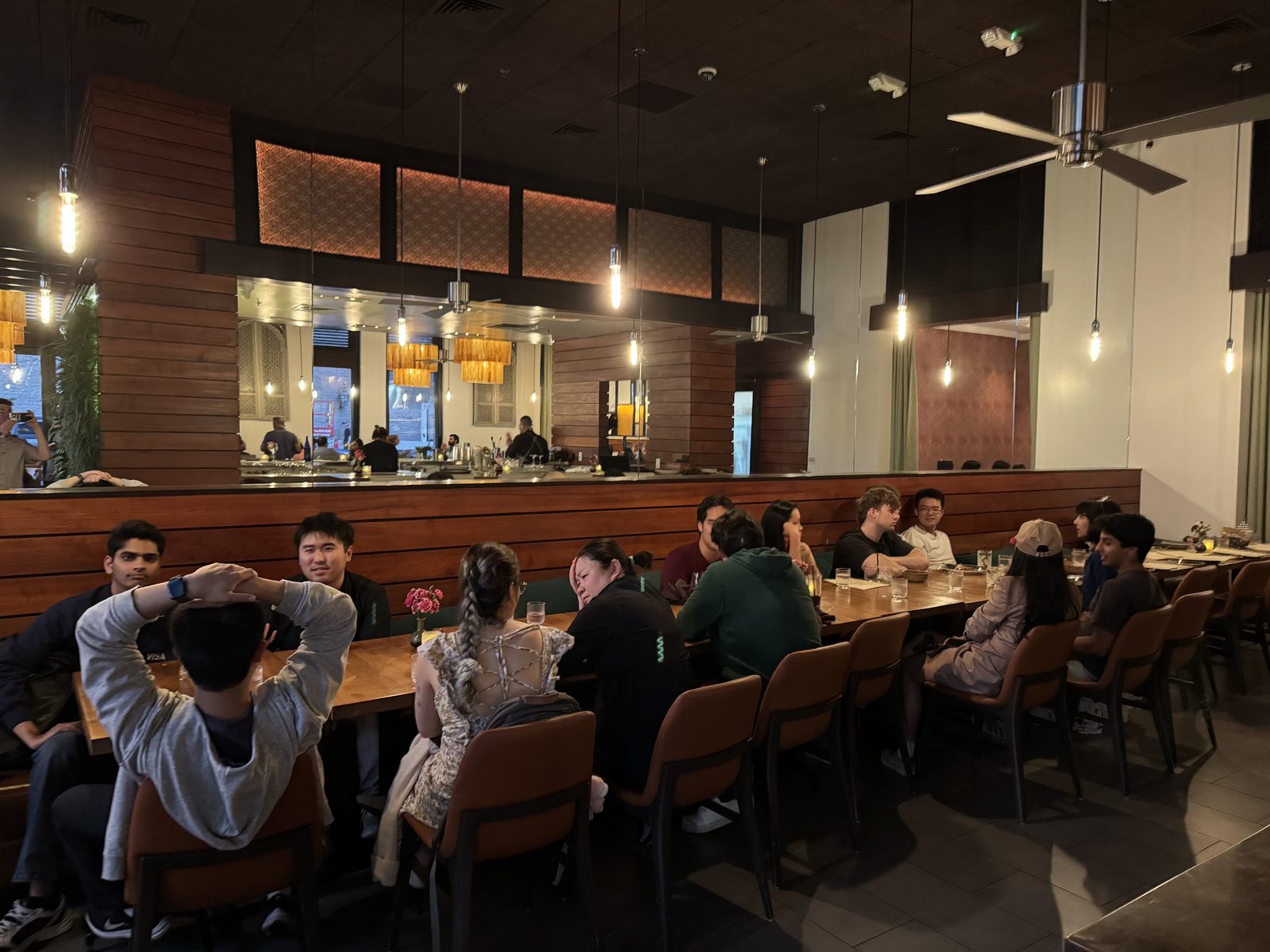 A long table of guests talking in a restaurant with wood paneling and pendant lights