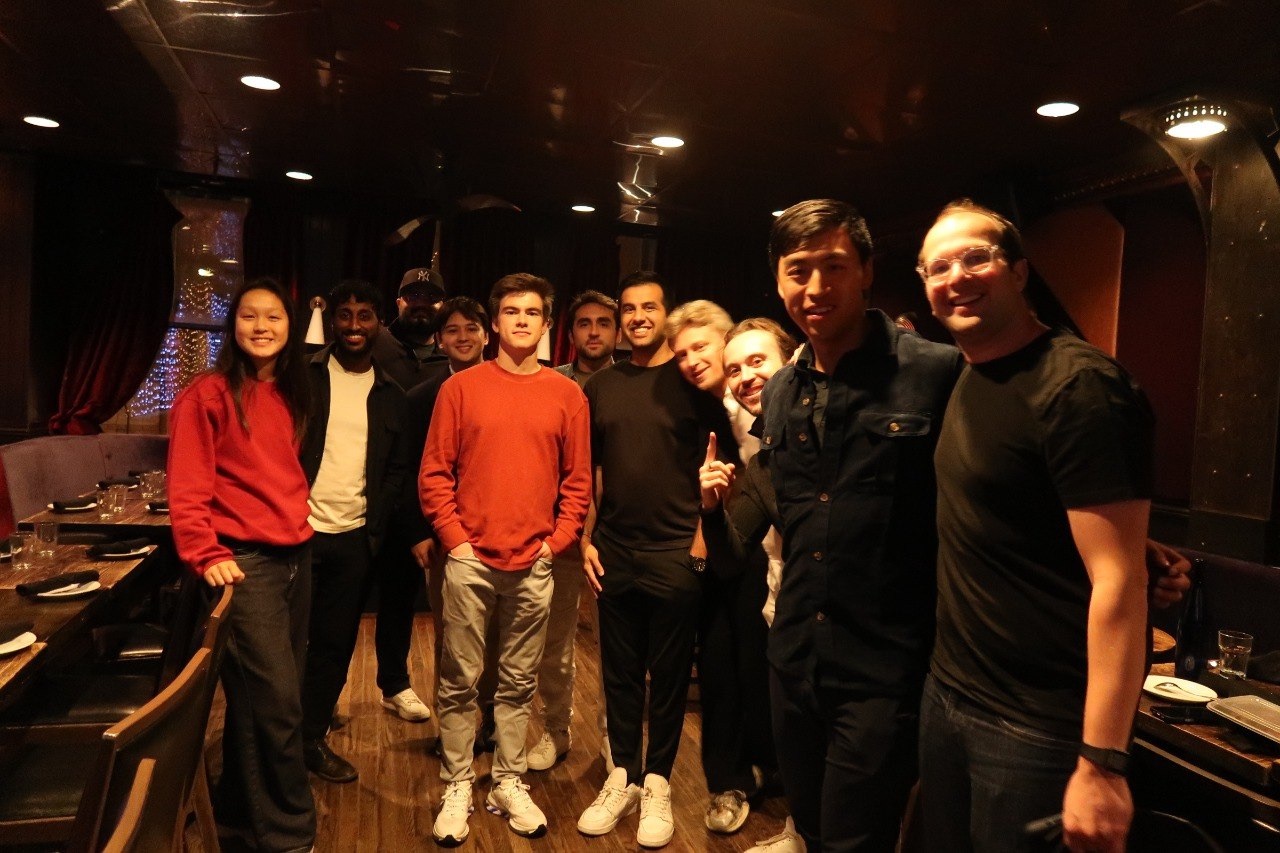 About a dozen people posing together in a dimly lit restaurant