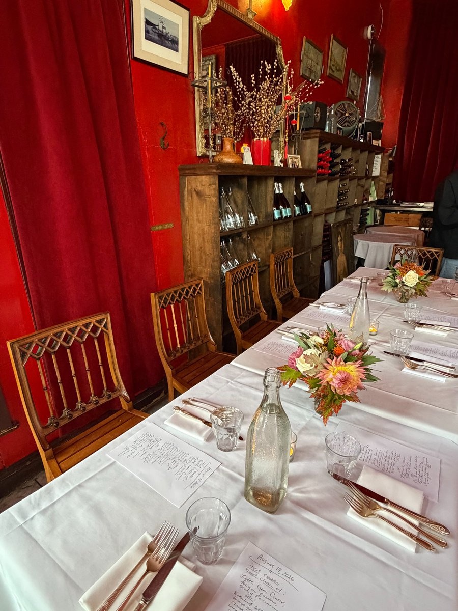 A long table set with white linens, flowers and handwritten menus in a red dining room