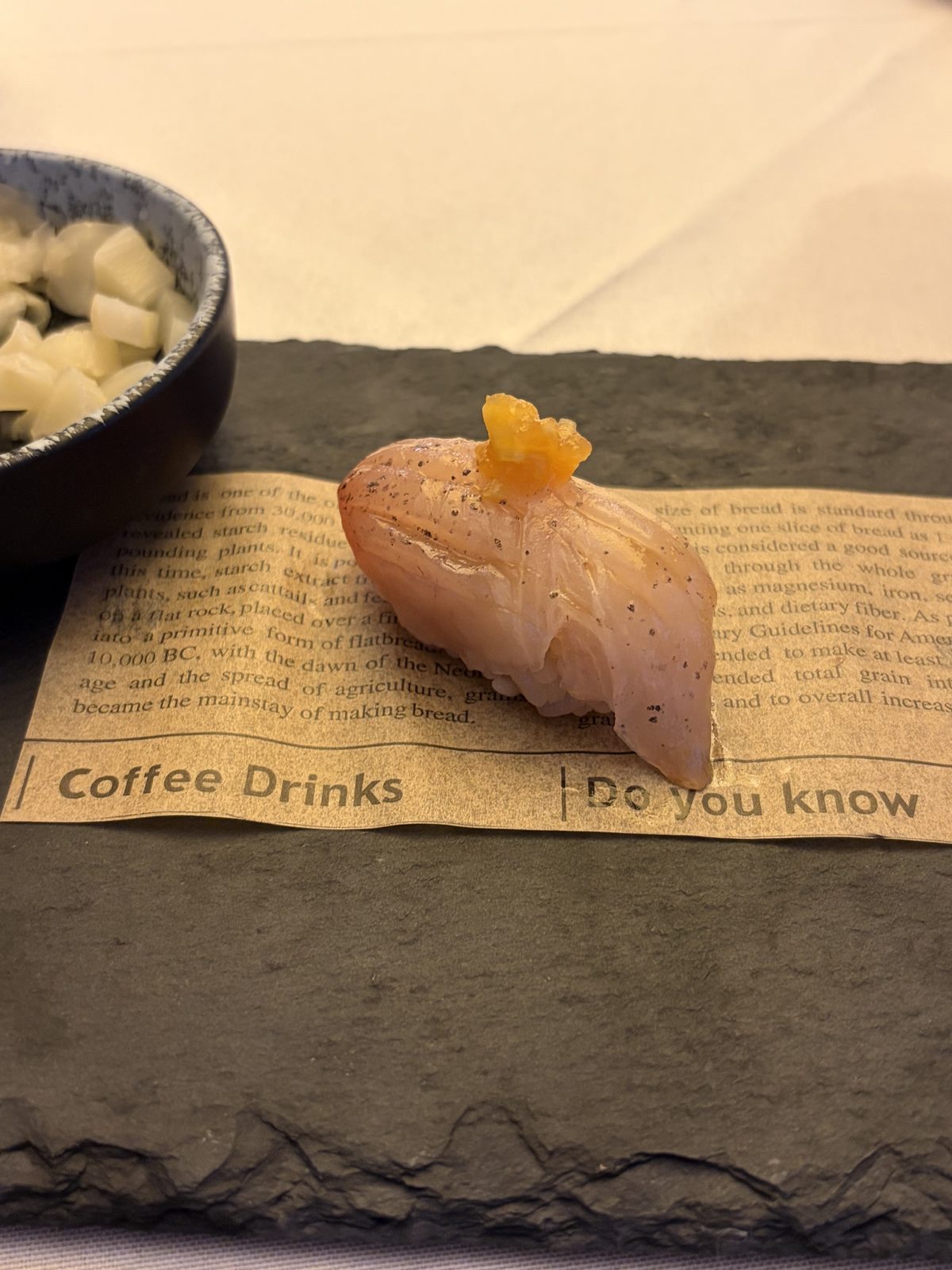 A piece of seared nigiri topped with citrus on a slate plate