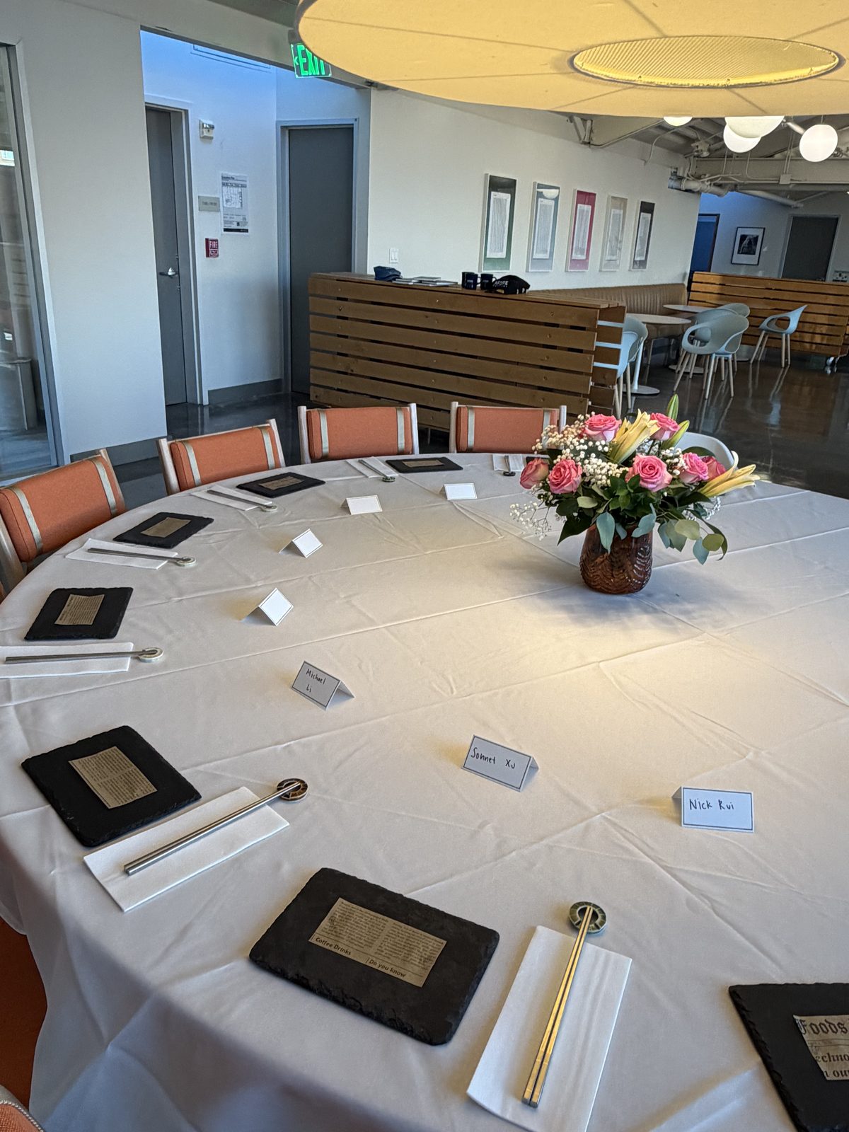 A round table set with slate plates, chopsticks, name cards and pink roses